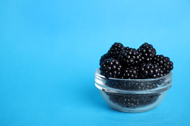 Photo of Fresh ripe blackberries in glass bowl on light blue background. Space for text