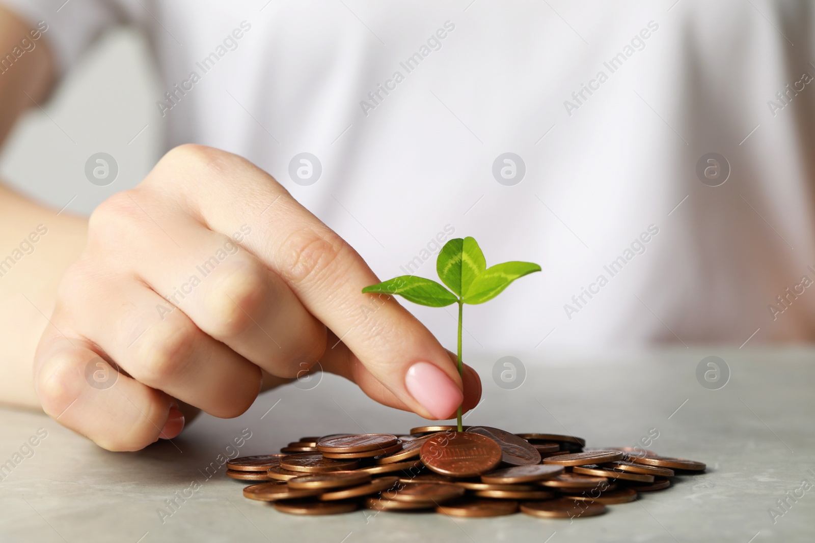 Photo of Woman putting green sprout onto pile of coins at grey table, closeup. Investment concept