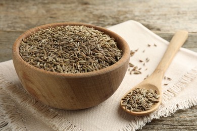 Bowl of caraway seeds and spoon on wooden table, closeup