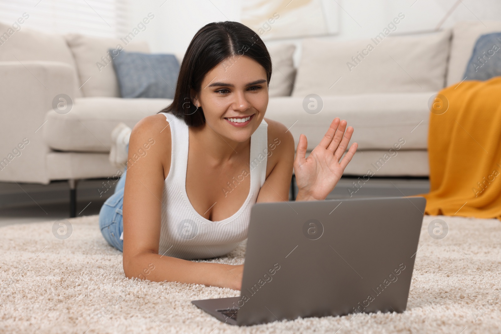 Photo of Happy young woman having video chat via laptop on floor in living room