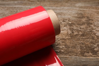 Photo of Roll of red plastic stretch wrap on wooden background, closeup. Space for text