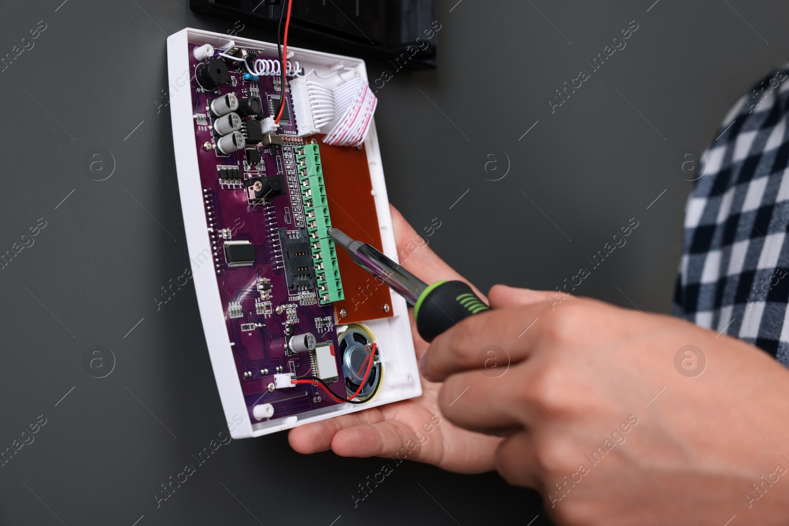 Photo of Man installing home security alarm system on gray wall, closeup