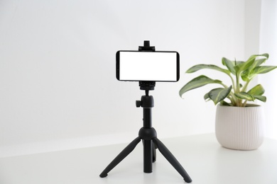 Photo of Smartphone with blank screen fixed to tripod on white table indoors. Mockup for design