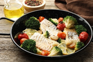 Photo of Tasty cod cooked with vegetables in frying pan on wooden table, closeup