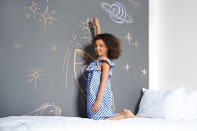 African-American child drawing rocket with chalk on wall in bedroom