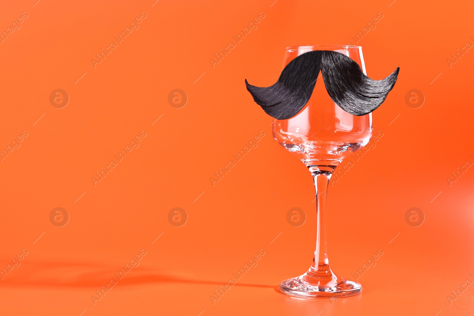 Photo of Man's face made of artificial mustache and wine glass on orange background. Space for text