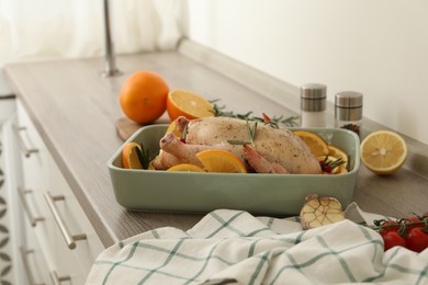 Photo of Chicken with orange slices in baking pan on wooden countertop