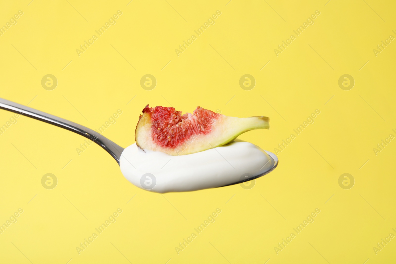 Photo of Spoon with yogurt and fig on yellow background, closeup