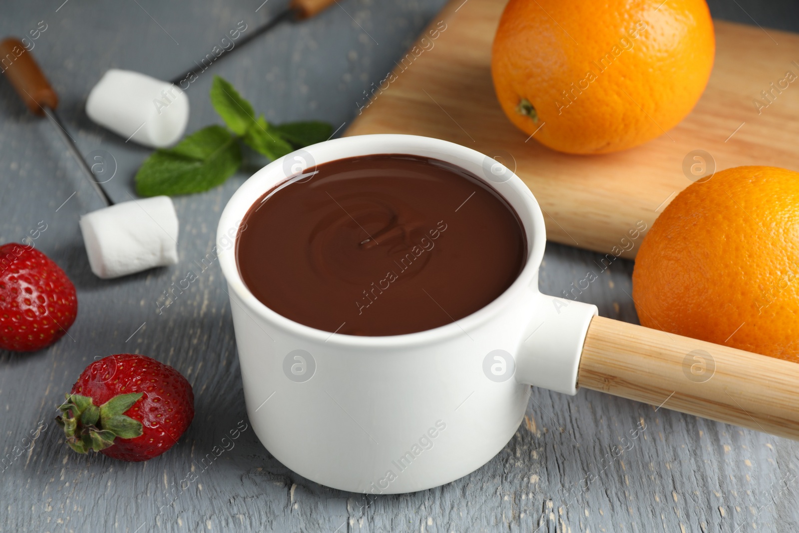 Photo of Fondue pot with chocolate, fruits and marshmallow on grey wooden table