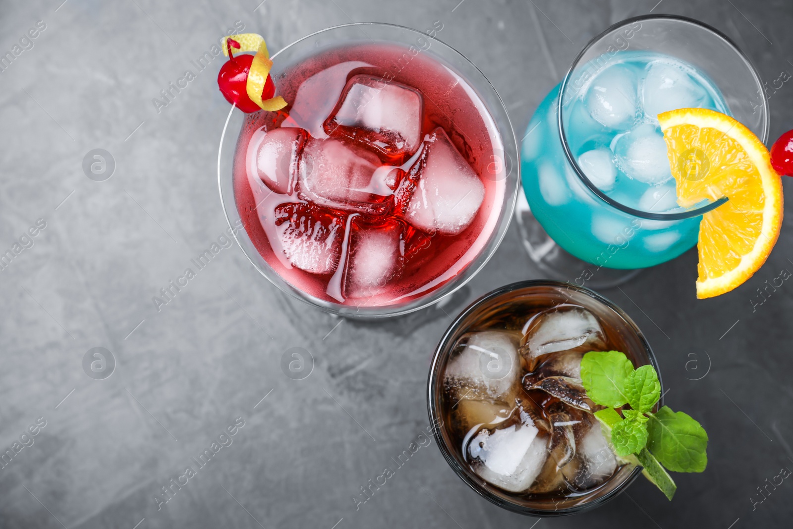 Photo of Tasty refreshing cocktails in glasses on grey stone table, flat lay. Space for text