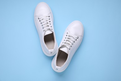 Photo of Pair of stylish white sneakers on light blue background, top view