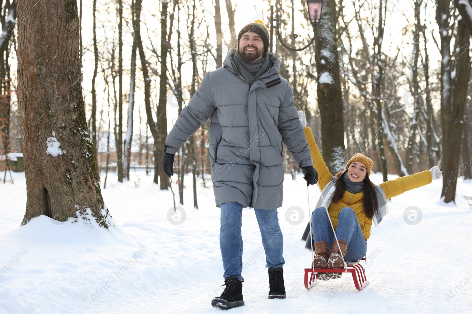 Photo of Happy young man pulling his girlfriend in sleigh outdoors on winter day