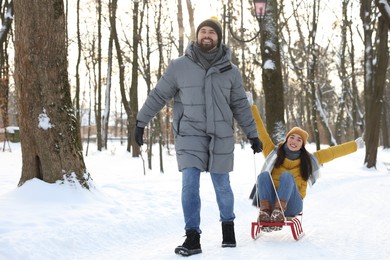 Happy young man pulling his girlfriend in sleigh outdoors on winter day