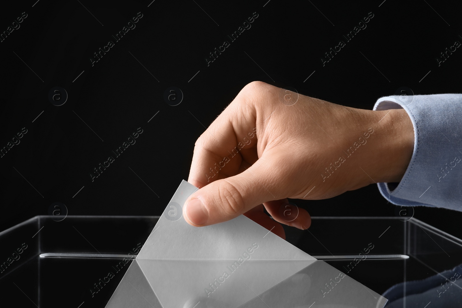 Photo of Man putting his vote into ballot box on black background, closeup