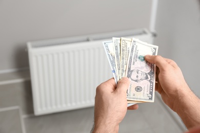 Photo of Man holding money near heating radiator indoors
