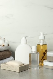Photo of Bath accessories. Personal care products, terry towels and cotton flowers on gray table near white marble wall