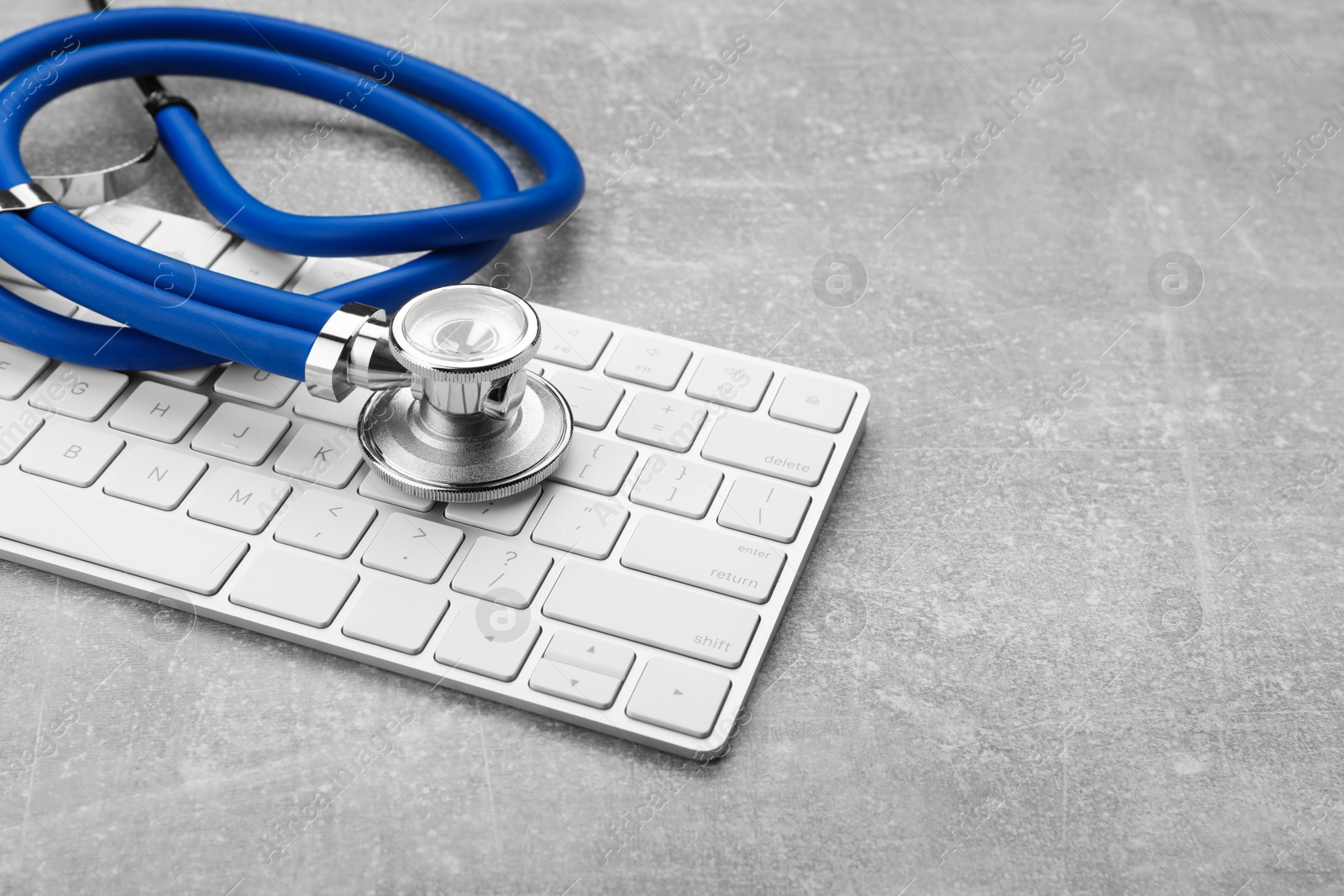 Photo of Computer keyboard with stethoscope on grey table, closeup. Space for text
