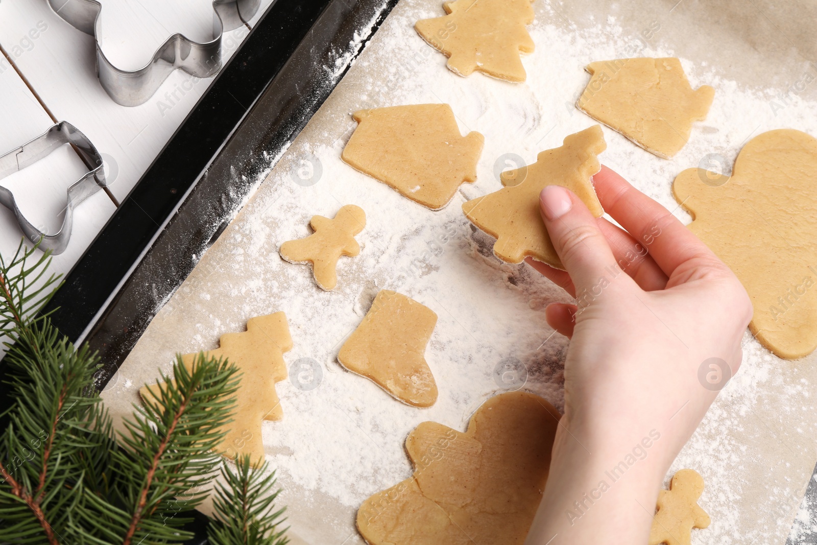 Photo of Woman putting raw Christmas cookies on baking tray at white table, closeup