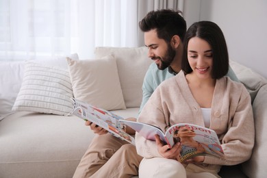 Photo of Young couple reading modern magazines on sofa at home, space for text