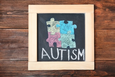 Photo of Chalkboard with word AUTISM and drawn puzzle pieces on wooden background