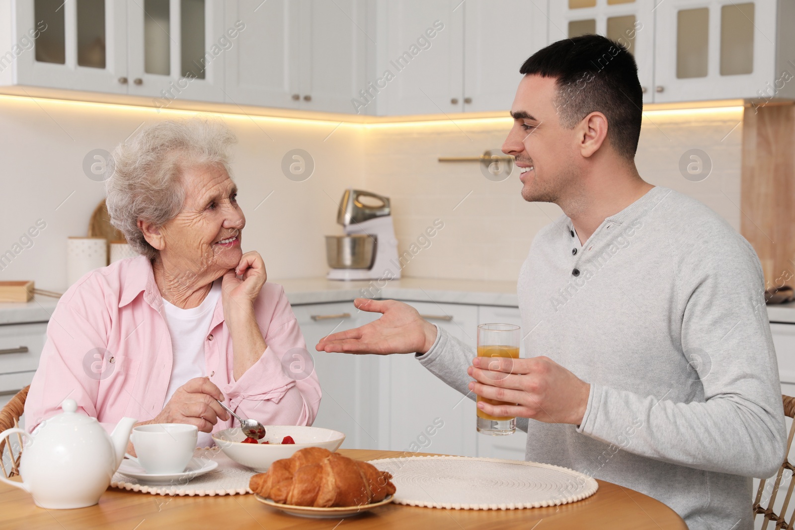 Photo of Young caregiver serving breakfast for senior woman at table in kitchen. Home care service