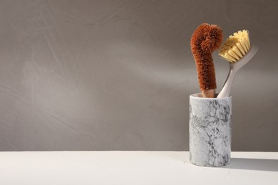 Photo of Cleaning brushes in holder on white table, closeup. Space for text