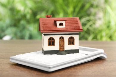 Mortgage concept. House model and calculator on wooden table against blurred green background, closeup