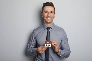 Male real estate agent with house model on grey background