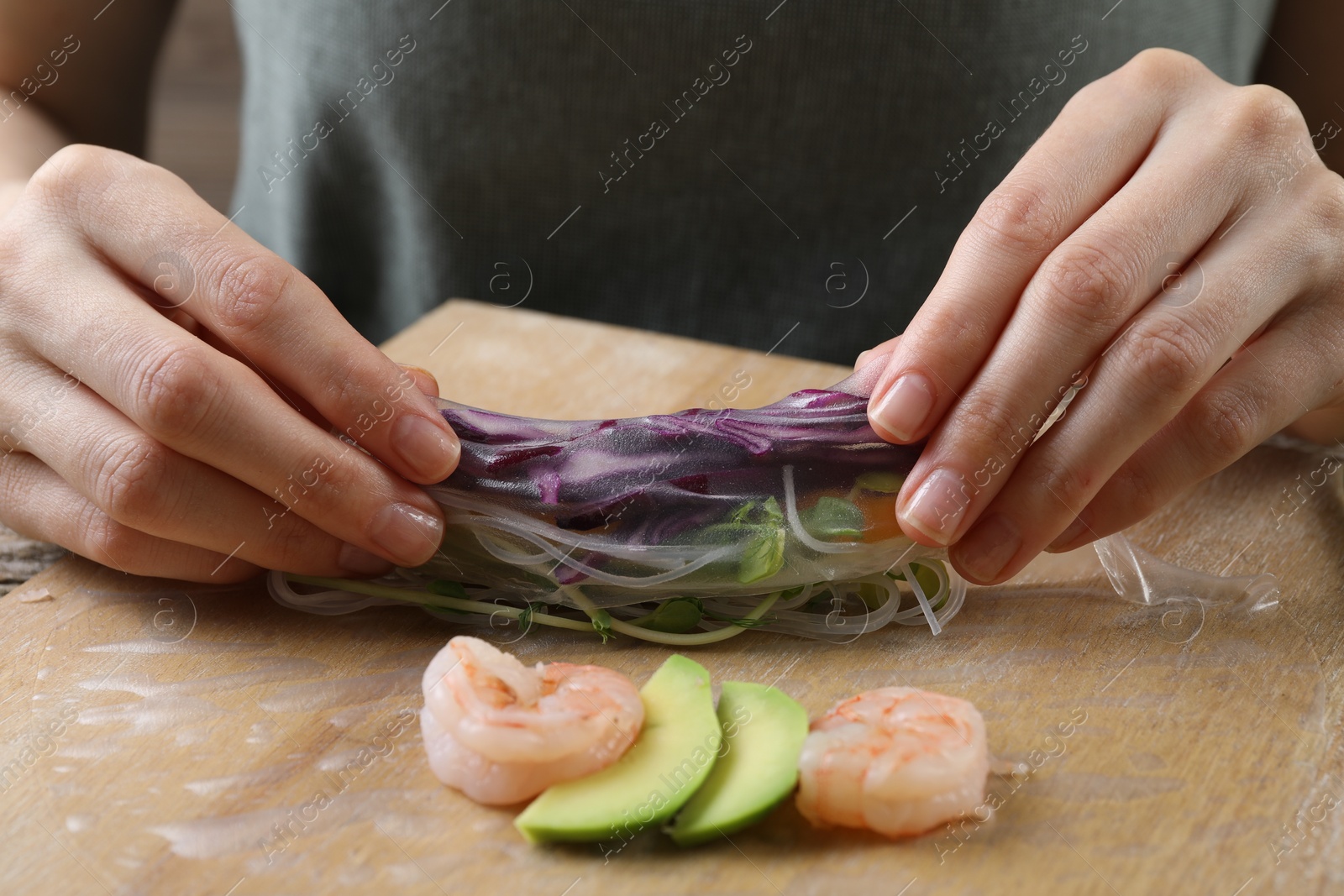 Photo of Woman wrapping spring roll at table with products, closeup