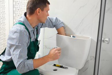 Professional plumber repairing toilet bowl in bathroom