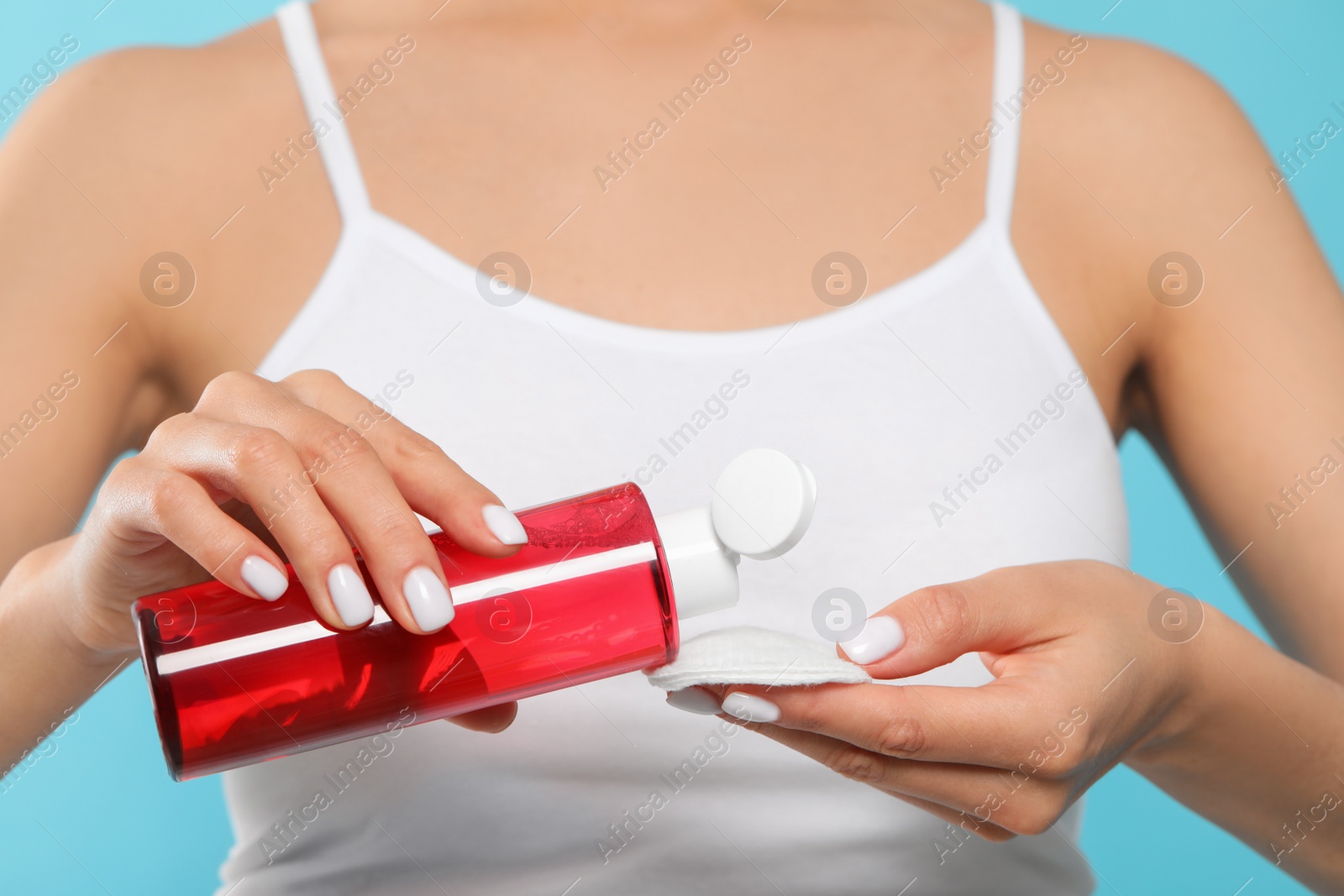 Photo of Woman pouring micellar water onto cotton pad on light blue background, closeup