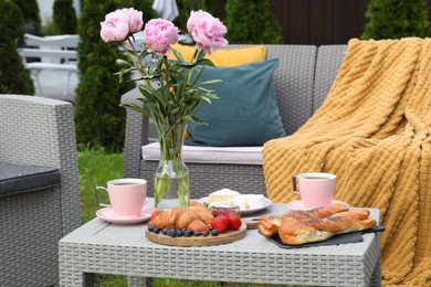 Photo of Morning drink, pastry, berries, cheese and vase with flowers on rattan table. Summer breakfast outdoors