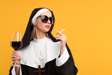 Photo of Woman in nun habit holding glass of wine and cigarette against orange background. Space for text