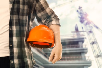 Image of Man with orange hard hat at construction site with unfinished building, closeup. Space for text 