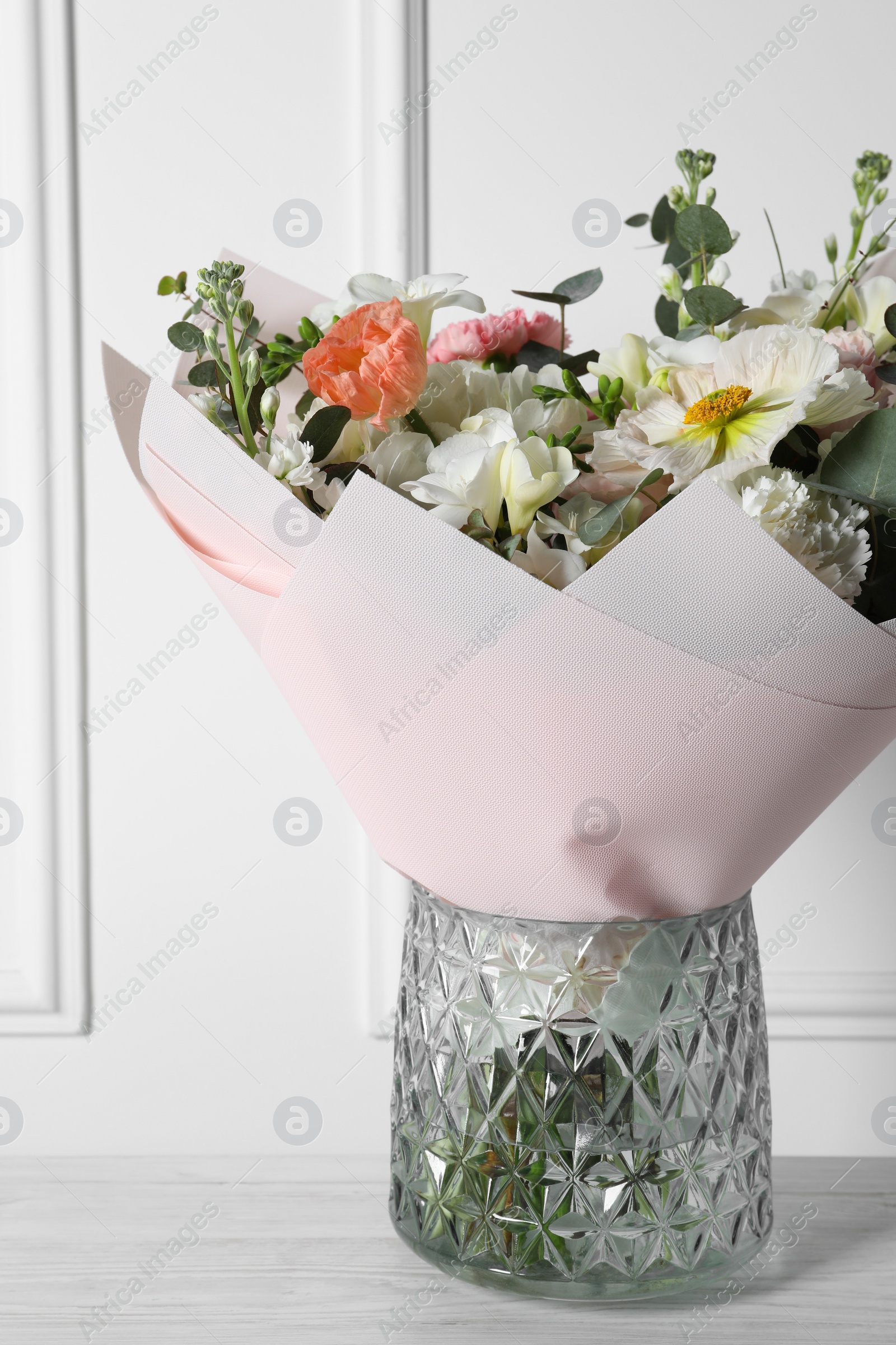 Photo of Bouquet of beautiful flowers in vase on wooden table against white wall