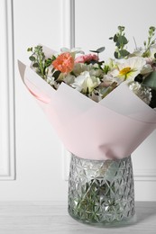 Bouquet of beautiful flowers in vase on wooden table against white wall