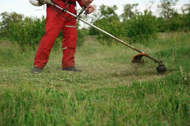 Photo of Worker cutting grass with string trimmer outdoors, closeup view
