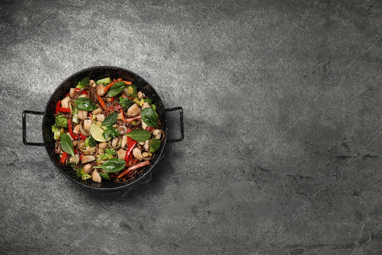 Photo of Stir-fry. Tasty noodles with meat and vegetables in wok on grey textured table, top view. Space for text