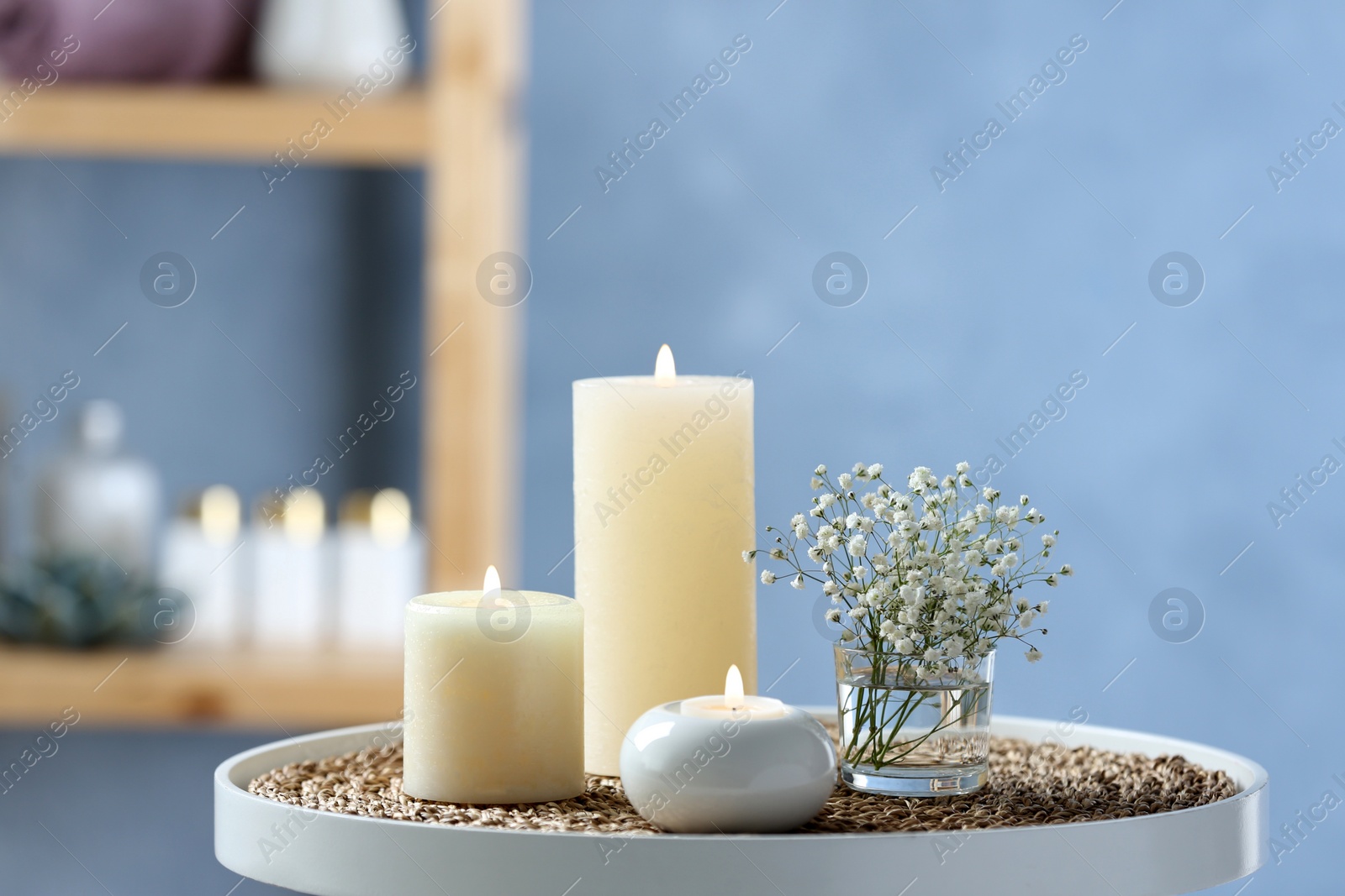 Photo of Burning candles and beautiful flowers on white table indoors