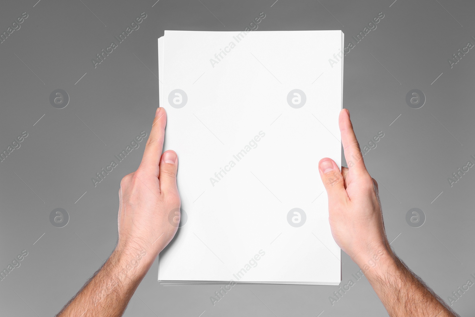 Photo of Man holding sheet of paper on grey background, closeup. Mockup for design