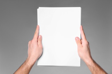 Man holding sheet of paper on grey background, closeup. Mockup for design