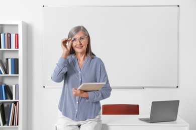 Portrait of professor with notebook near whiteboard in classroom