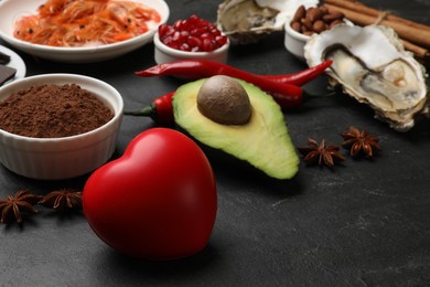Photo of Natural aphrodisiac. Different food products and heart model on black table, closeup