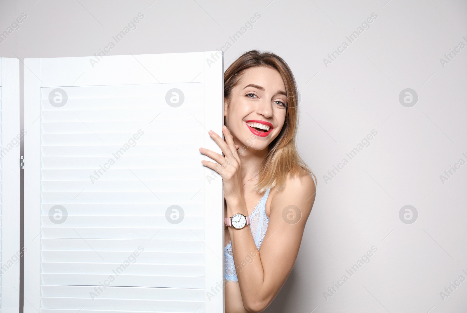 Photo of Young woman behind folding screen against light background, space for text. Dressing room