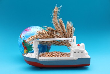 Globe, ears of wheat, toy cargo vessel on light blue background. Import and export concept