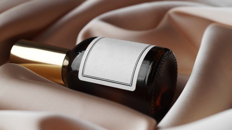 Photo of Luxury bottle of perfume on beige silk, closeup