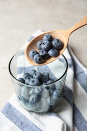 Photo of Spoon with juicy and fresh blueberries over glass on color table