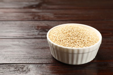 Photo of Dry quinoa seeds in bowl on wooden table, space for text