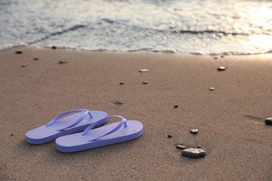 Photo of Stylish lilac flip flops on sand near sea. Space for text