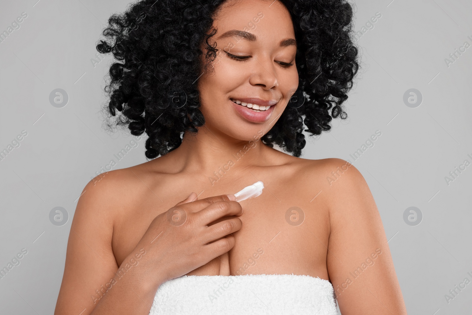 Photo of Young woman applying cream onto body on grey background